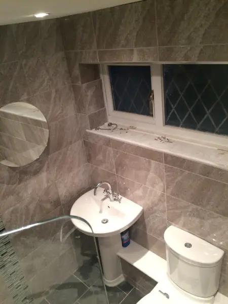 Stone-effect tiled bathroom with basin, illuminated mirror and chrome fittings